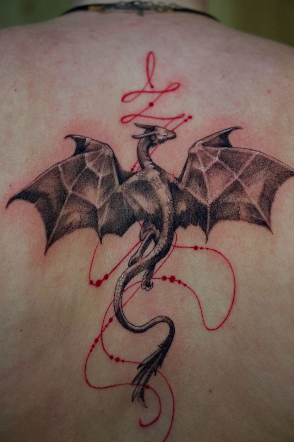 fine line dragon back tattoo with red accents by Antwan Rodriguez, West Palm Beach FL